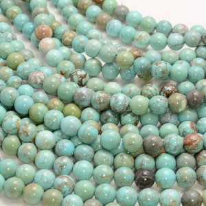 May include: A strand of turquoise beads, each bead is round and has a mottled blue-green color with brown and white markings.