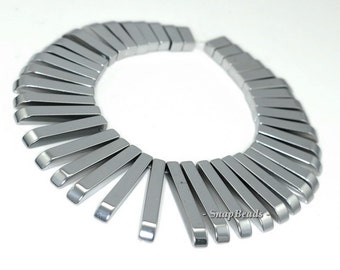 May include: A strand of silver-colored metal beads, each bead is a long, thin rectangle with rounded edges. The beads are arranged in a circle, with the ends of the beads overlapping.