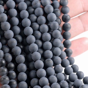 May include: A strand of dark gray matte round beads. The beads are smooth and have a slightly textured surface.