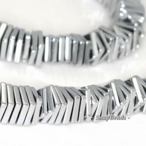 May include: A strand of silver and white rectangular beads. The beads are stacked on top of each other, creating a layered effect. The beads are smooth and shiny.