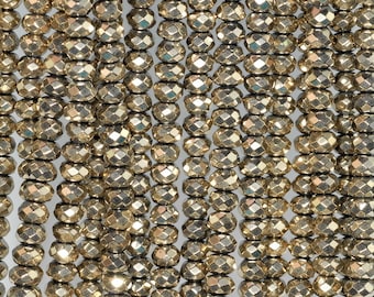 May include: Close-up of multiple strands of faceted, golden-colored beads. The beads have a metallic sheen and are strung together, creating a textured surface. The beads are oval-shaped and have a geometric, multi-faceted design.
