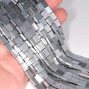 May include: A strand of silver hematite beads, each bead is a rectangular prism with a smooth, polished finish.