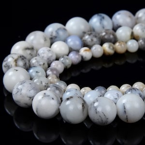 May include: A strand of white and gray opal beads with black dendritic inclusions. The beads are round and smooth, and they are arranged in a circle.