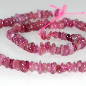May include: A strand of pink tourmaline beads, each bead is a unique, irregular shape. The beads are strung on a pink thread.