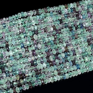 May include: A strand of faceted green and blue fluorite beads. The beads are round and have a translucent appearance. The beads are strung on a clear thread.