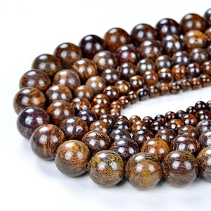 May include: A strand of brown and gold round gemstone beads. The beads are various sizes and have a speckled pattern.