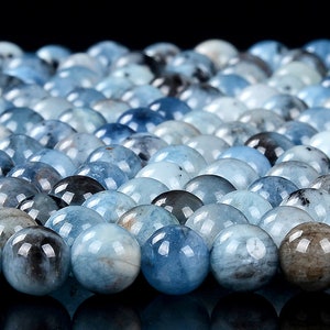 May include: A close-up of a collection of round, light blue aquamarine beads. The beads are smooth and polished, with a slight variation in color and pattern.