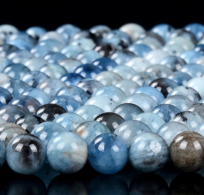 May include: A close-up of a collection of round, light blue aquamarine beads. The beads are smooth and polished, with a slight variation in color and pattern.
