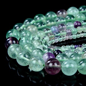 May include: A strand of green and purple fluorite beads. The beads are round and smooth, and they have a translucent appearance. The beads are strung on a clear thread.