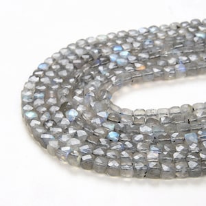 May include: A strand of gray faceted labradorite beads. The beads are square shaped and have a shimmery iridescent finish.