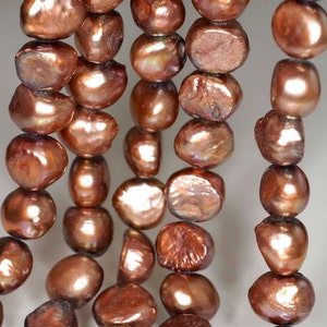 Könnte beinhalten: Eine Strähne brauner Süßwasserperlen mit einem leicht schillernden Glanz. Die Perlen sind unregelmäßig geformt und haben ein natürliches, organisches Aussehen.