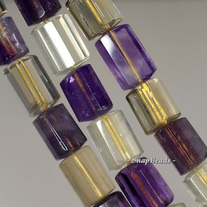 Puede incluir: Una hebra de cuentas de piedras preciosas facetadas en tonos de morado, marrón y transparente. Las cuentas son de forma rectangular y tienen una raya de color dorado que recorre el centro.