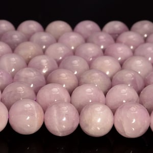 May include: A close-up of a strand of round, pale pink beads. The beads are smooth and have a slight sheen.