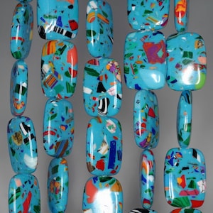 Puede incluir: Una hebra de cuentas rectangulares de color azul turquesa con motas e inclusiones de colores. Las cuentas están enhebradas en un cordón transparente.