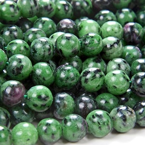 May include: Close-up of a strand of green and black gemstone beads. The beads are round and have a speckled appearance.