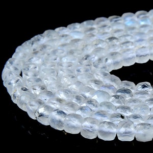 May include: A strand of white moonstone beads, faceted and polished, with a subtle iridescent sheen. The beads are arranged in a circular pattern, showcasing their smooth, rounded surfaces.