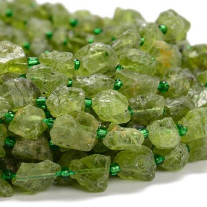 May include: A strand of green peridot gemstone beads with green spacer beads. The peridot beads are rough and irregular in shape.