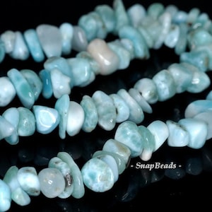 May include: A strand of light blue and white gemstone beads. The beads are irregular in shape and have a smooth, polished finish. The beads are strung on a clear thread and are arranged in a loose, flowing pattern.