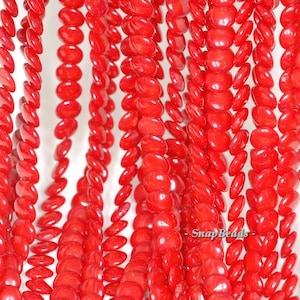 May include: A strand of bright red oval-shaped beads. The beads are smooth and glossy, and they are strung together on a clear thread.