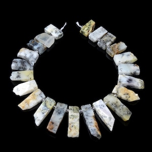 Könnte beinhalten: Eine Kette aus weißen, grauen und grünen dendritischen Opalperlen. Die Perlen sind rechteckig und haben eine natürliche, raue Textur. Die Perlen sind auf einer weißen Schnur aufgefädelt.