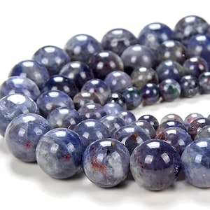 Puede incluir: Una hebra de cuentas redondas de piedras preciosas azules y moradas. Las cuentas son lisas y tienen un acabado ligeramente iridiscente.
