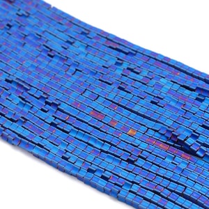 Può includere: Una fila di perline quadrate blu e viola. Le perline sono in metallo e hanno una finitura lucida.