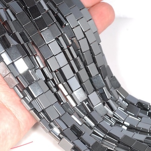 Peut inclure: Un brin de perles d'hématite carrées de couleur argent et noire. Les perles sont facettées et ont un éclat métallique.