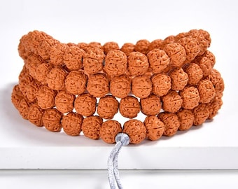 Puede incluir: Tres pulseras hechas de cuentas marrones texturizadas. Las cuentas están ensartadas y sujetas por un cordón gris. Las pulseras se exhiben sobre una superficie blanca.