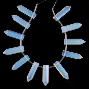 May include: A strand of 14 iridescent opal gemstone beads, each shaped like a pointed rectangle, strung on a clear elastic cord. The beads are a pale blue color with a slight shimmer.