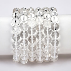 May include: A stack of five clear quartz crystal bead bracelets. Each bracelet is made of round, smooth beads.