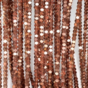 May include: Close-up of multiple strands of copper-colored, faceted beads. The beads are strung together, creating vertical lines against a white background. The beads have a metallic sheen, reflecting light and adding a touch of elegance. Ideal for jewelry making.