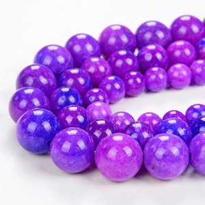 May include: A strand of purple and lavender round beads made of natural stone. The beads are smooth and polished, with a slight variation in color and texture.