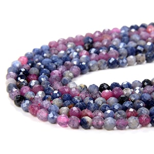 May include: A strand of faceted gemstone beads in shades of blue, pink, and purple. The beads are round and have a slightly irregular shape.