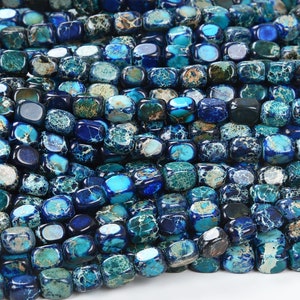 May include: A strand of blue and green jasper beads, each bead is a square with rounded edges. The beads are polished and have a mottled appearance.