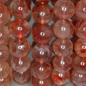 May include: A strand of round, translucent red and orange gemstone beads. The beads are smooth and polished, with a slight shimmer.