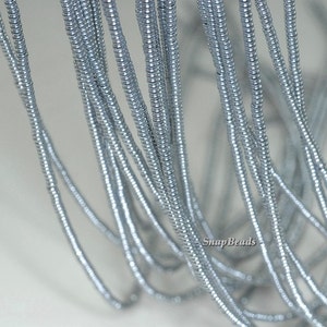 Könnte beinhalten: Nahaufnahme von silberfarbenen Metallperlen, die zu einer langen Schnur aufgefädelt sind. Die Perlen sind klein und rund und haben eine glänzende Oberfläche. Die Schnur liegt auf einer weißen Oberfläche. SnapBeads ist auf dem Bild aufgedruckt.