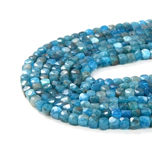May include: A strand of blue gemstone beads, each bead is faceted and has a square shape.