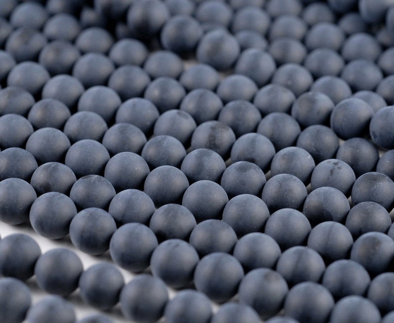 May include: A strand of dark gray round beads. The beads are smooth and matte.
