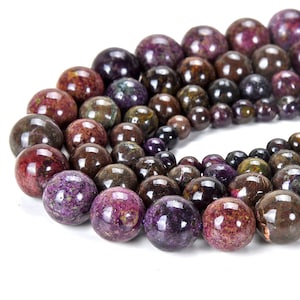 May include: A strand of round, purple and brown gemstone beads. The beads are smooth and have a speckled appearance.