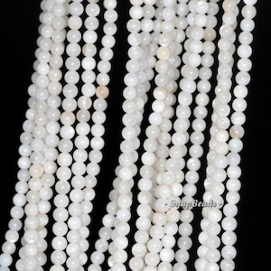 May include: A strand of white round beads made from mother of pearl. The beads are smooth and have a slight iridescent sheen.