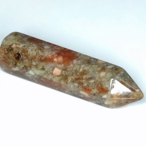 May include: A polished, elongated stone pendant with a pointed end and a drilled hole. The stone features a mix of colors, including reddish-brown, beige, and gray, with a speckled pattern. The pendant is smooth and appears to be made of natural stone.