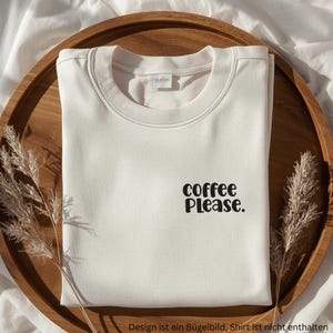 Puede incluir: Una sudadera de cuello redondo color crema con el texto negro "coffee Please." impreso en la parte superior derecha del pecho. La prenda tiene un cuello acanalado y un diseño estándar de manga larga, presentada de forma plegada.