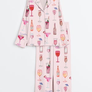 Peut inclure: Ensemble de pyjama rose clair avec un motif r&eacute;p&eacute;t&eacute; de verres &agrave; cocktails, de bouteilles et de garnitures. Le haut &agrave; manches longues a une fermeture boutonn&eacute;e et le pantalon est droit. L'ensemble est en mati&egrave;re douce et soyeuse.