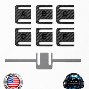 May include: Six black carbon fibre textured clips labelled A through F, arranged in two rows of three. Below them is a single grey flat metal tool with a central U-shaped cutout. Logos for Proudly Made in USA, UltiMaker, PF Audio Solutions, and Atomic Filament are visible at the bottom.