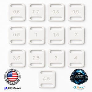 May include: A collection of thirteen white rectangular plastic clips, each featuring two horizontal slots and a debossed numerical value ranging from 0.5 to 4.5. The set includes a circular Proudly Made in USA badge and two company logos.