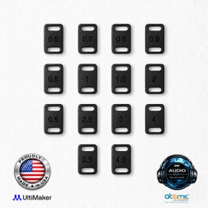 Peut inclure: Un ensemble de quatorze composants rectangulaires en plastique noir, chacun doté de deux fentes et d'une valeur numérique allant de 0,5 à 4,5. L'ensemble comprend un emblème circulaire Proudly Made in USA, un logo Ultimaker et un logo PF Audio Solutions.