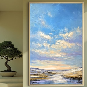 Könnte beinhalten: Ein Ölgemälde einer Landschaft mit einem hellblauen Himmel voller flauschiger weißer Wolken. Der Vordergrund zeigt ein Gewässer mit sanften Hügeln und goldenen Feldern in der Ferne. Das Kunstwerk ist in einem goldfarbenen Rahmen gerahmt.