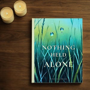 May include: A hardcover book titled "NOTHING HELD ALONE" with a cover illustration of green grass and water droplets. Two lit candles are in the background on a dark wooden surface.