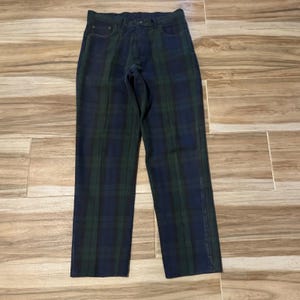 May include: Full-length trousers featuring a dark navy blue and forest green plaid tartan pattern. These pants include a standard waistband with belt loops, a front button closure, a zippered fly, and two front pockets with visible stitching details.