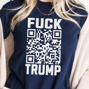 Puede incluir: Camiseta azul marino con las palabras "FUCK TRUMP" en letras blancas sobre un diseño de código QR. La camiseta es de cuello redondo.